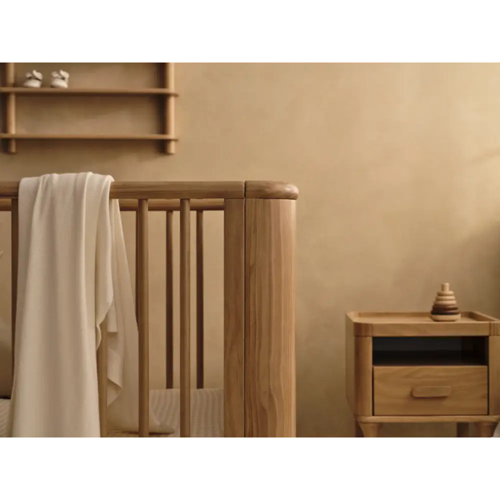 Wooden baby crib with draped blanket from Tasman Eco Willow collection featuring willow 3-door chest