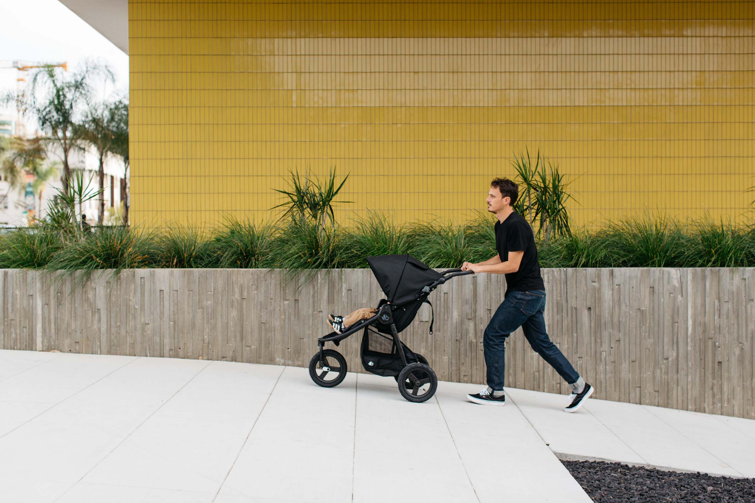 Man pushing a black Bumbleride Indie Stroller with Toshi Baby Romper, perfect baby strollers
