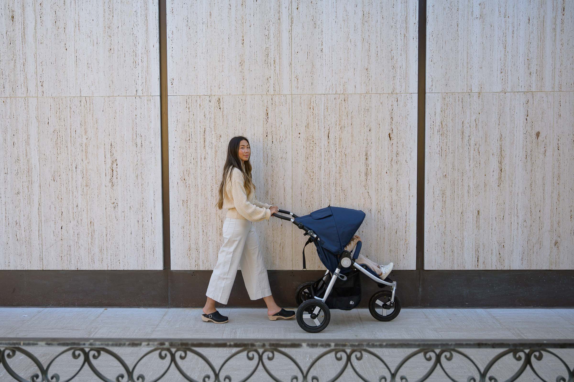 Woman pushing navy Bumbleride Indie Stroller with Toshi Baby Romper, best baby strollers