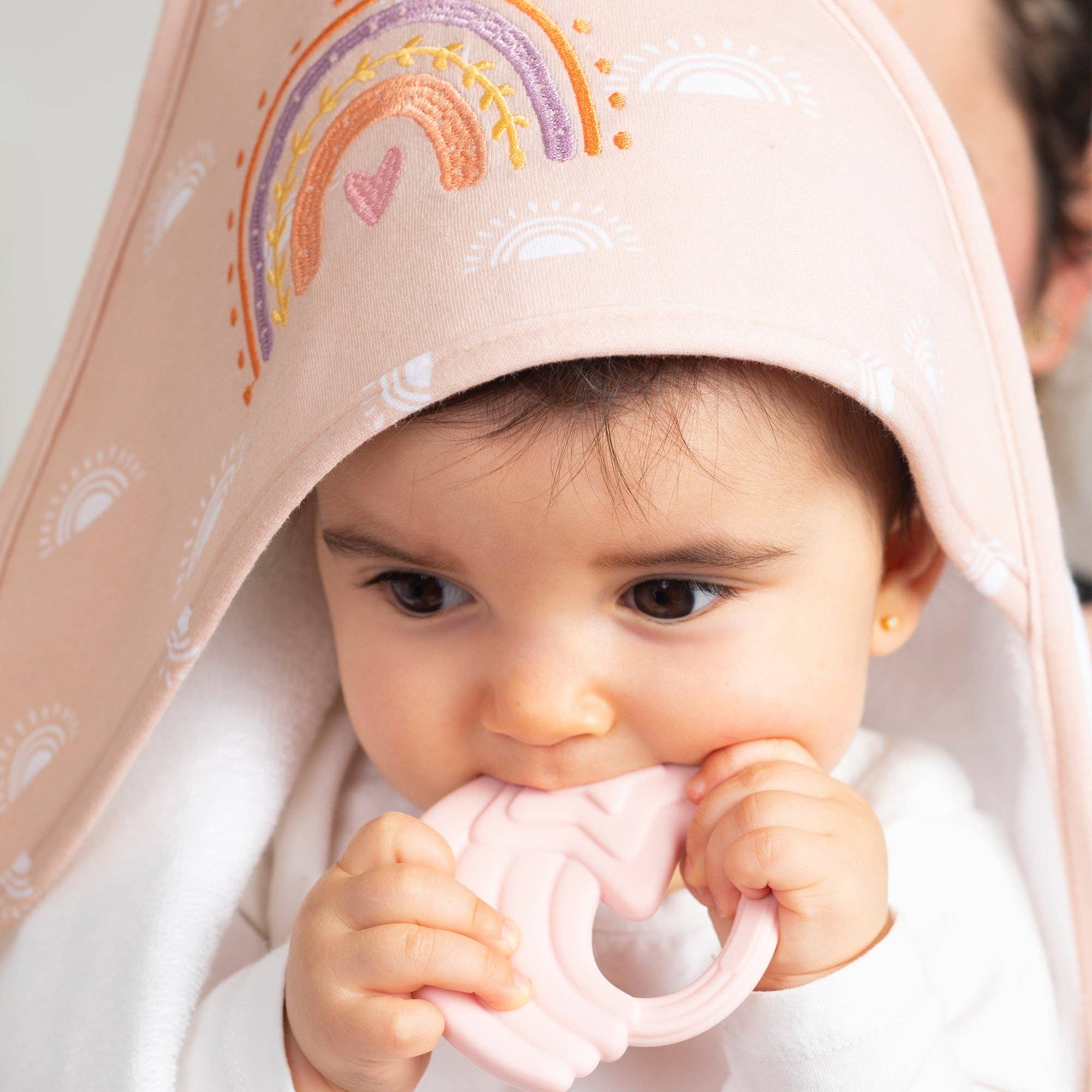 Baby chewing pink teether with Living Textiles Hooded Towel during baby’s bath time