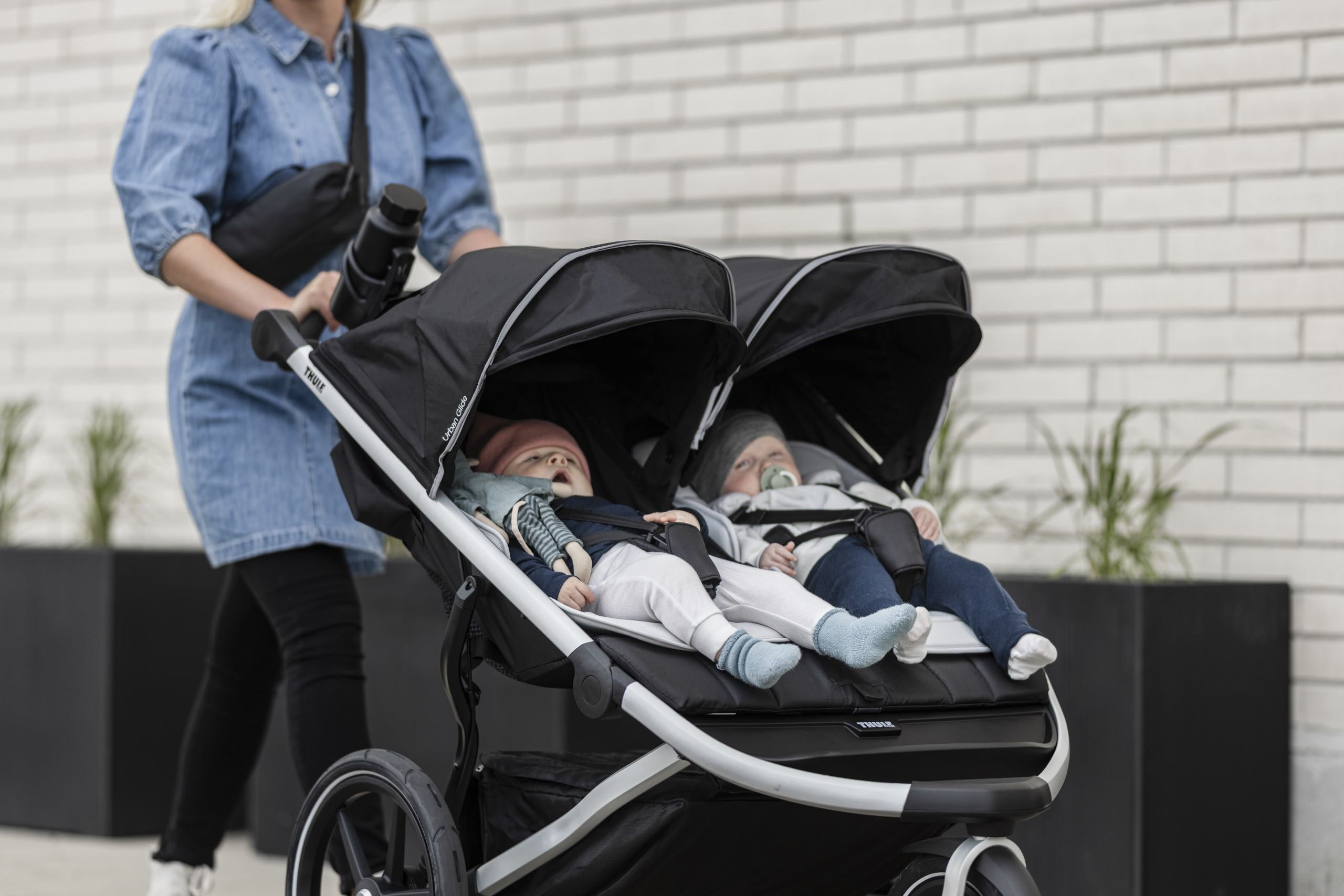 Black double stroller with two babies using Thule Newborn Inlay, perfect for Toshi baby romper and Thule Sunhat Odyssey