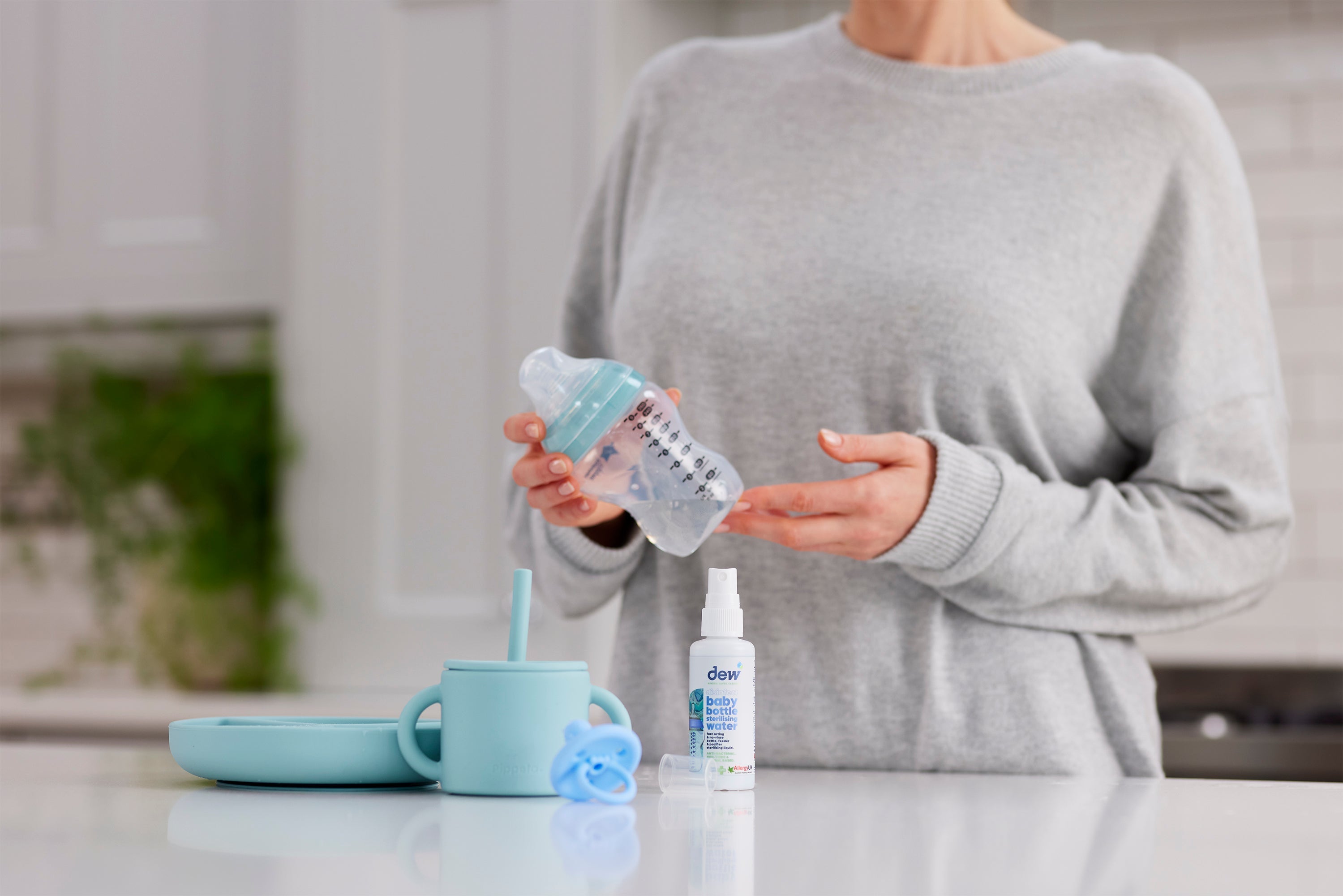 Baby bottle held by person with Dew Baby Bottle Sterilising Water 65ml for sterilising bottles