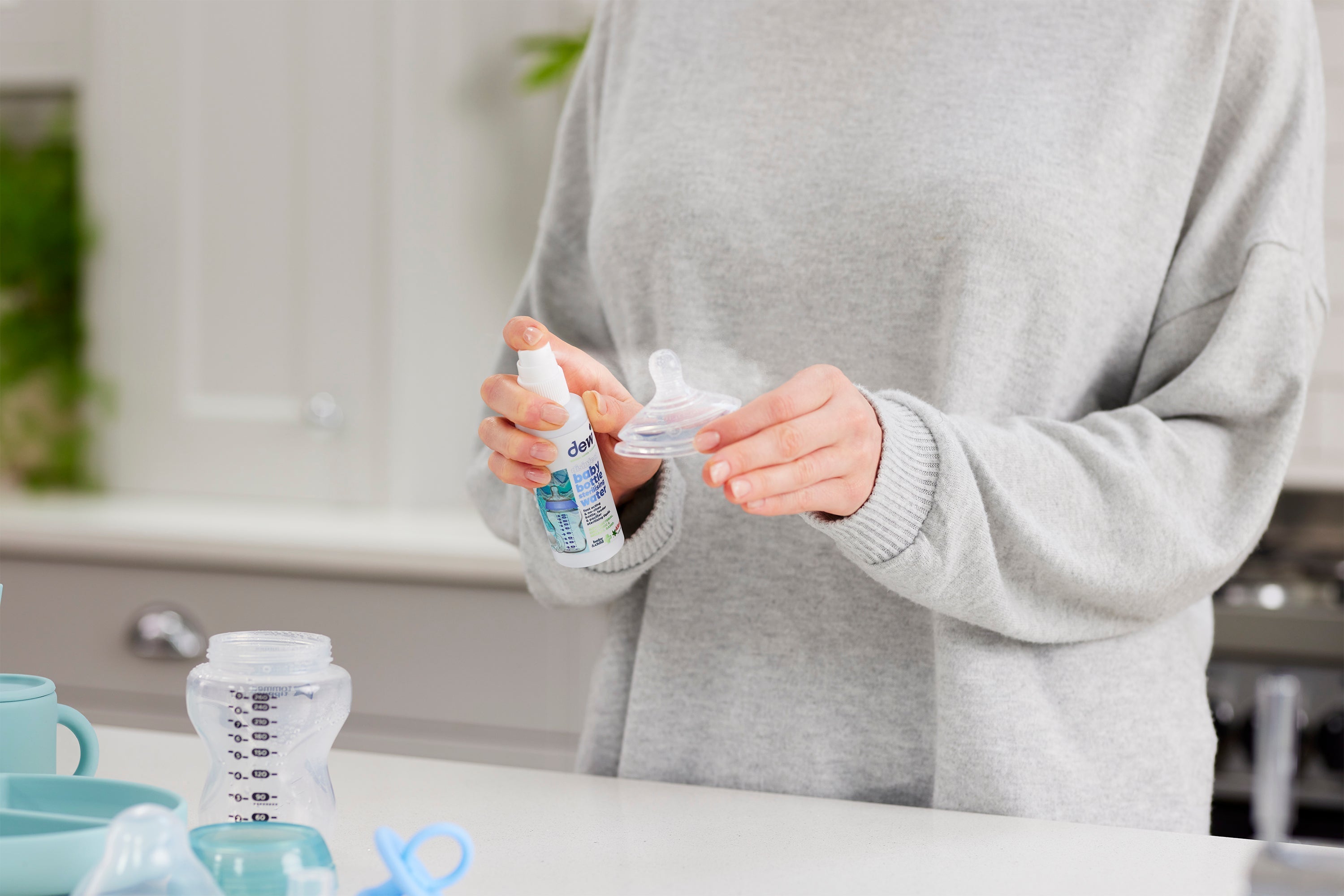 Person spraying Dew Baby Bottle Sterilising Water 65ml on a baby bottle nipple