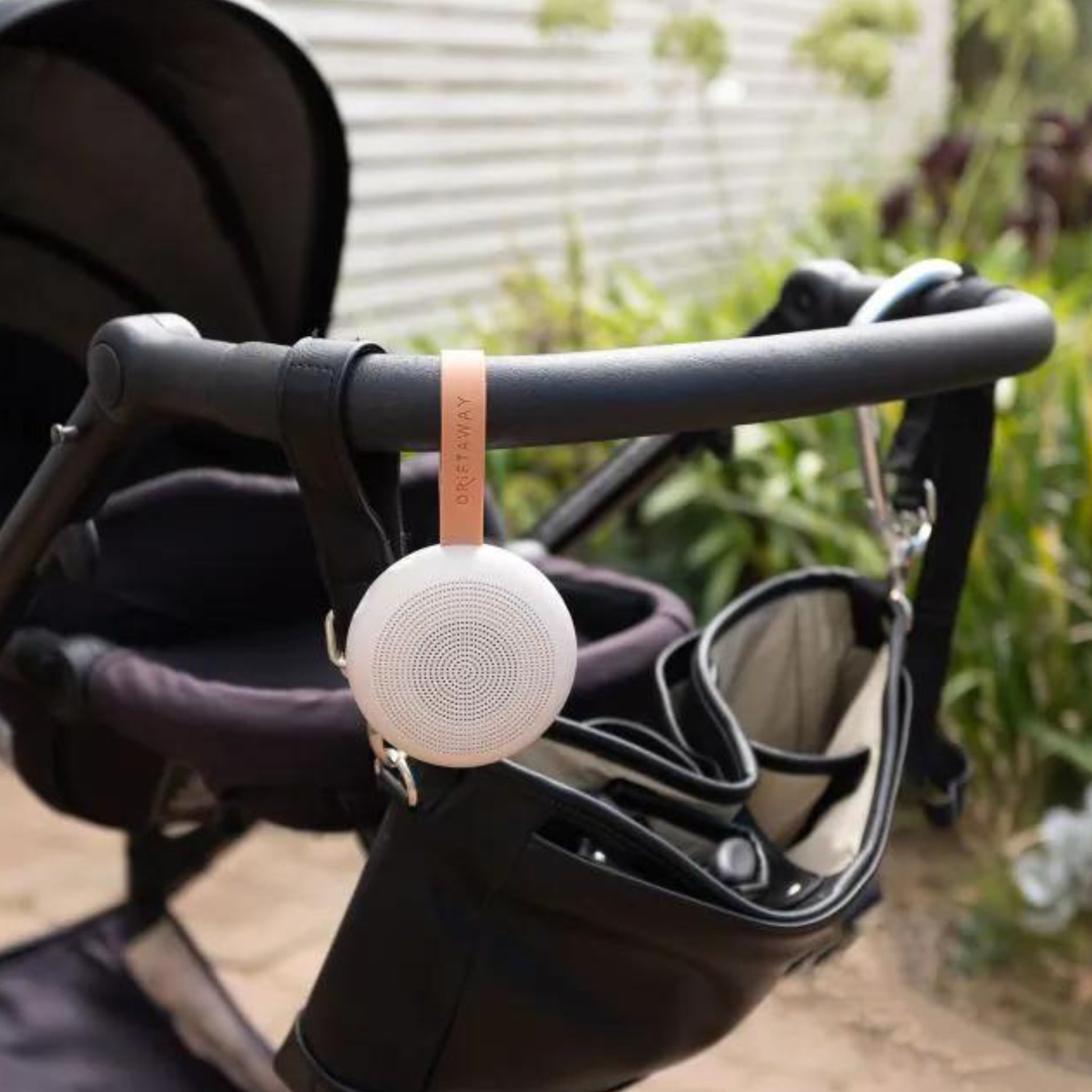 White circular portable white noise speaker hanging from a baby stroller for soothing sleep