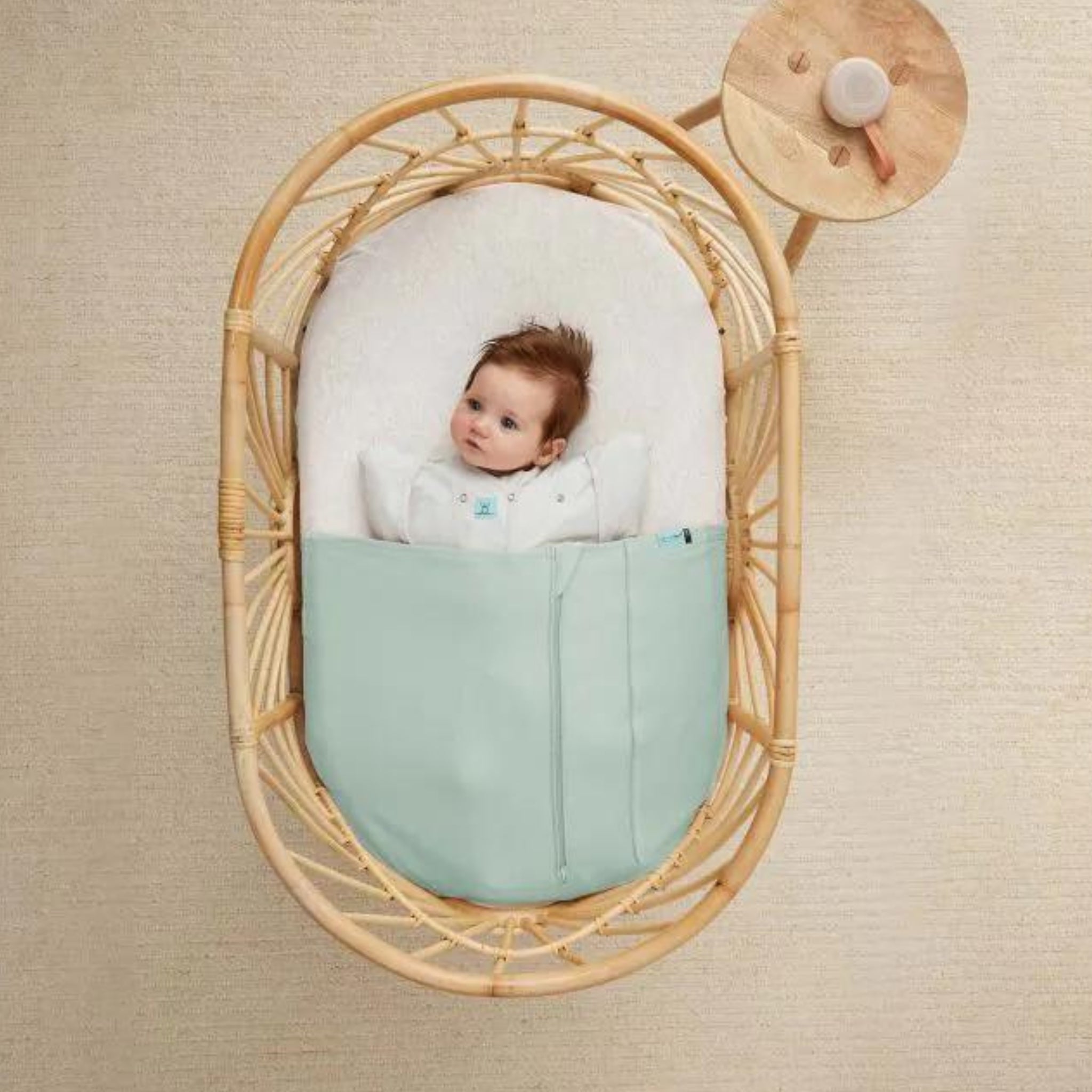 Baby in woven bassinet with light blue blanket using ErgoPouch Drift Away portable white noise machine