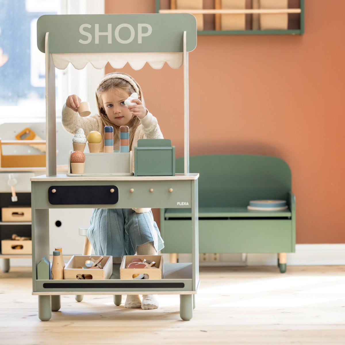 Child’s wooden play shop in Flexa Shop and Cafe with Toshi Baby Romper and Odyssey Wagon Wheels