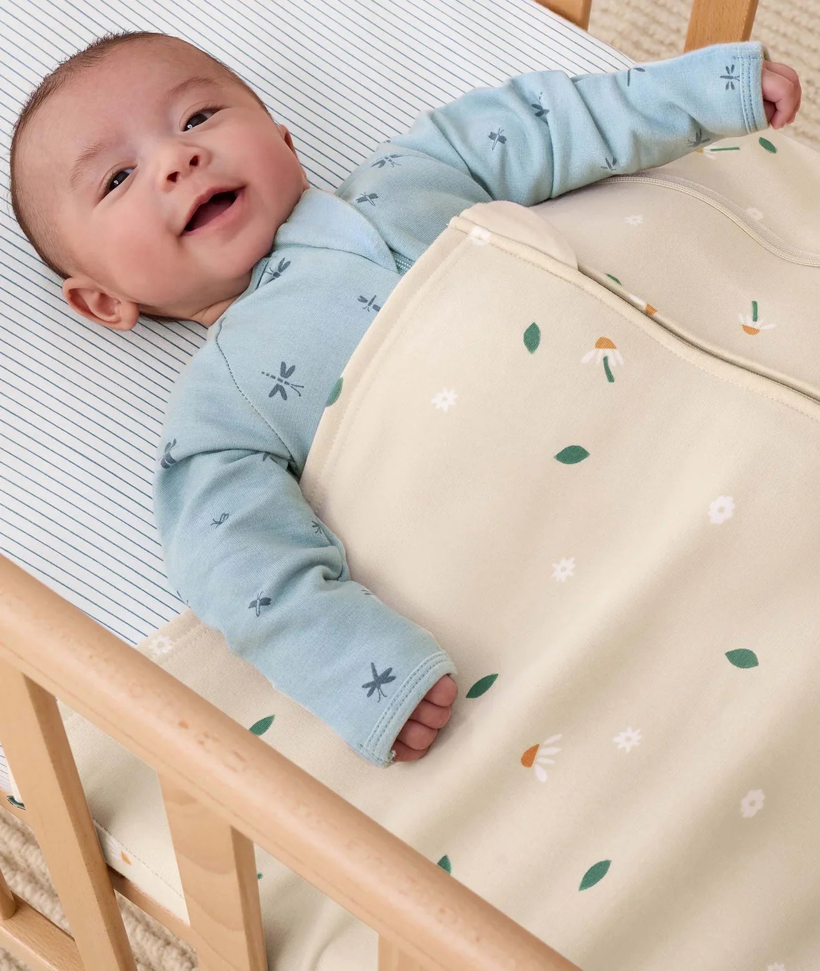 Smiling baby in patterned sleep sack with Ergopouch HugMe Blanket for comfy naps