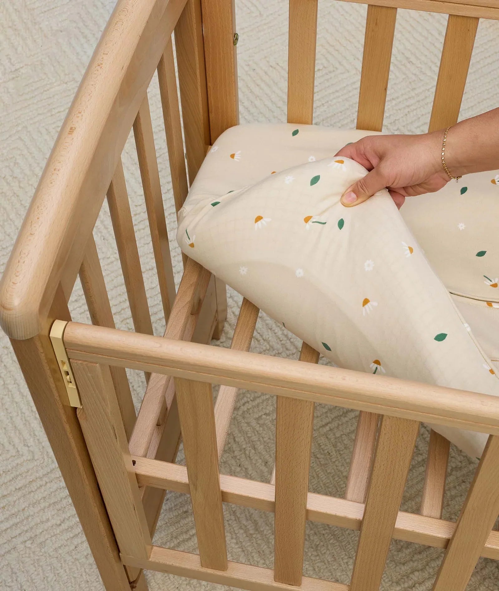 Wooden baby crib with floral sheet and Ergopouch HugMe Blanket for cozy cuddles
