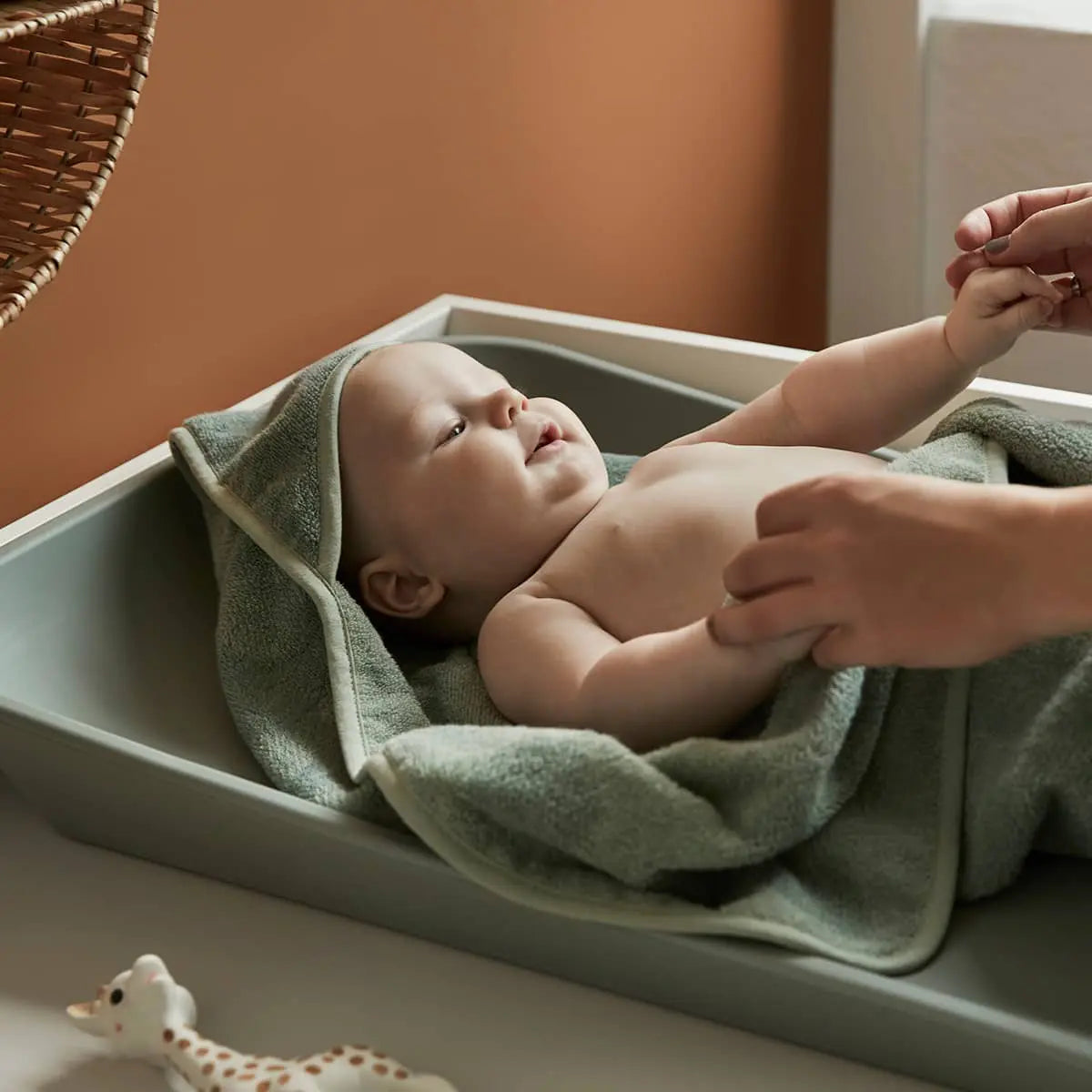 Toshi baby lying on a changing table with Leander Organic Hooded Towels, perfect for baby strollers