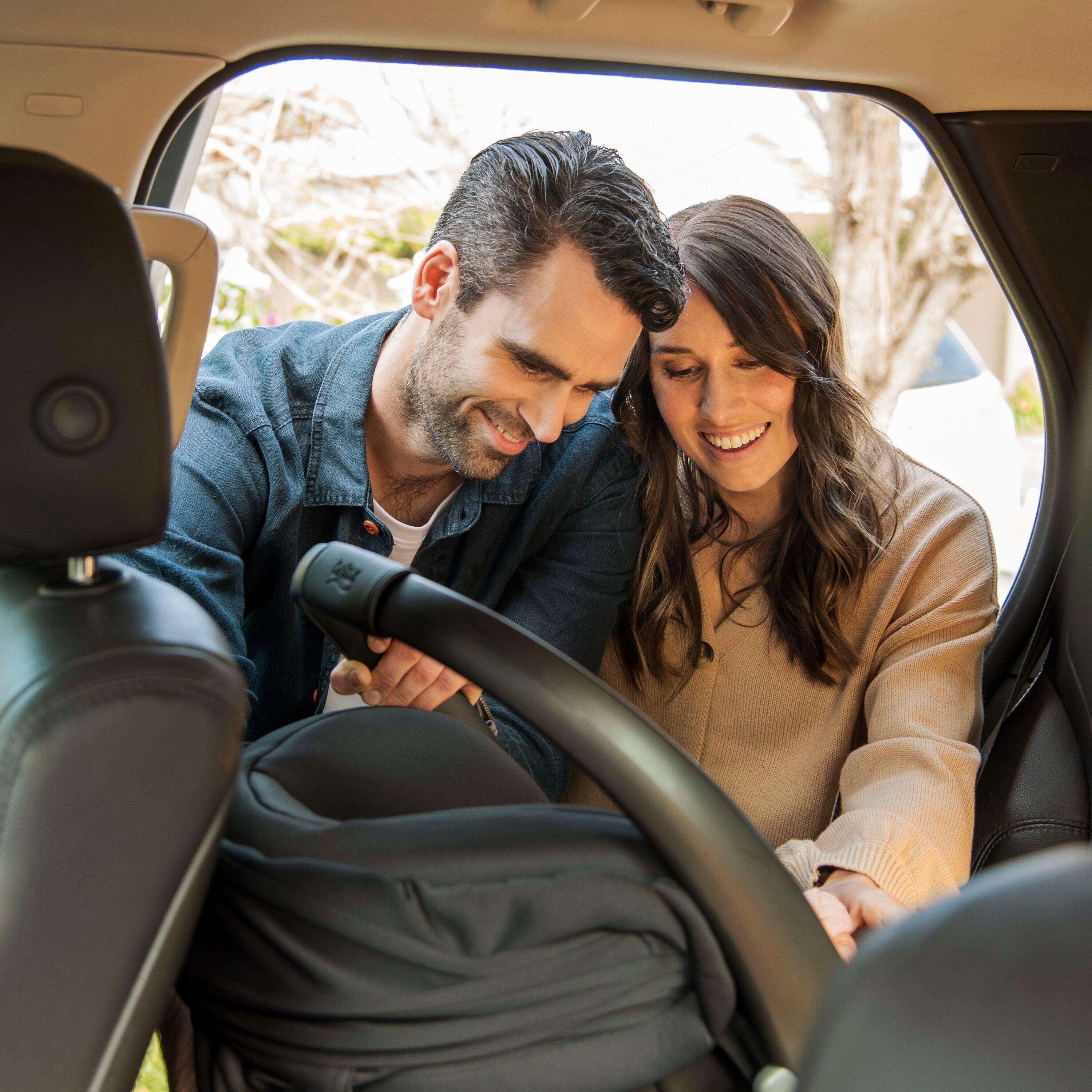 Couple installing Britax Safe-N-Sound B-Pod LITE Baby Capsule with Toshi Baby Romper near Odyssey Wagon Wheels and baby strollers