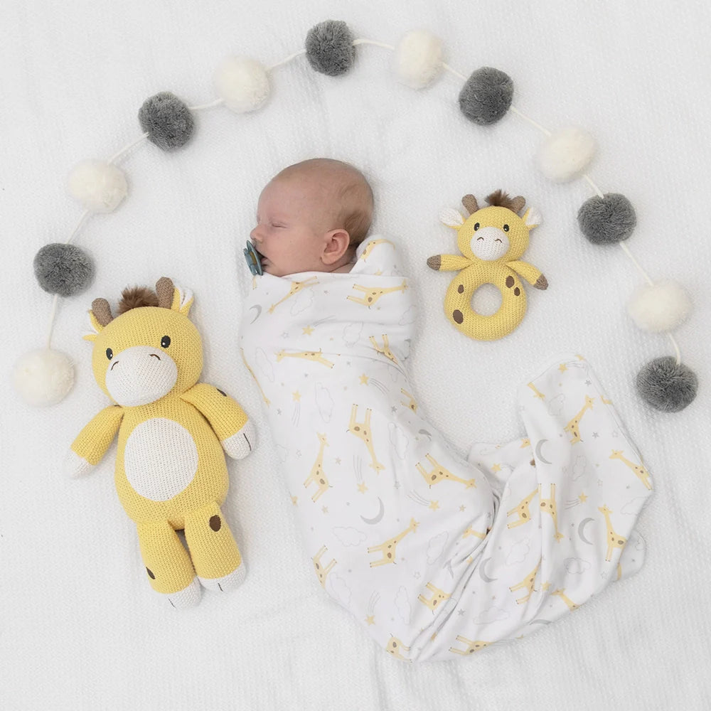 Swaddled baby with living textiles knitted giraffe soft toy and pompom garland in baby strollers