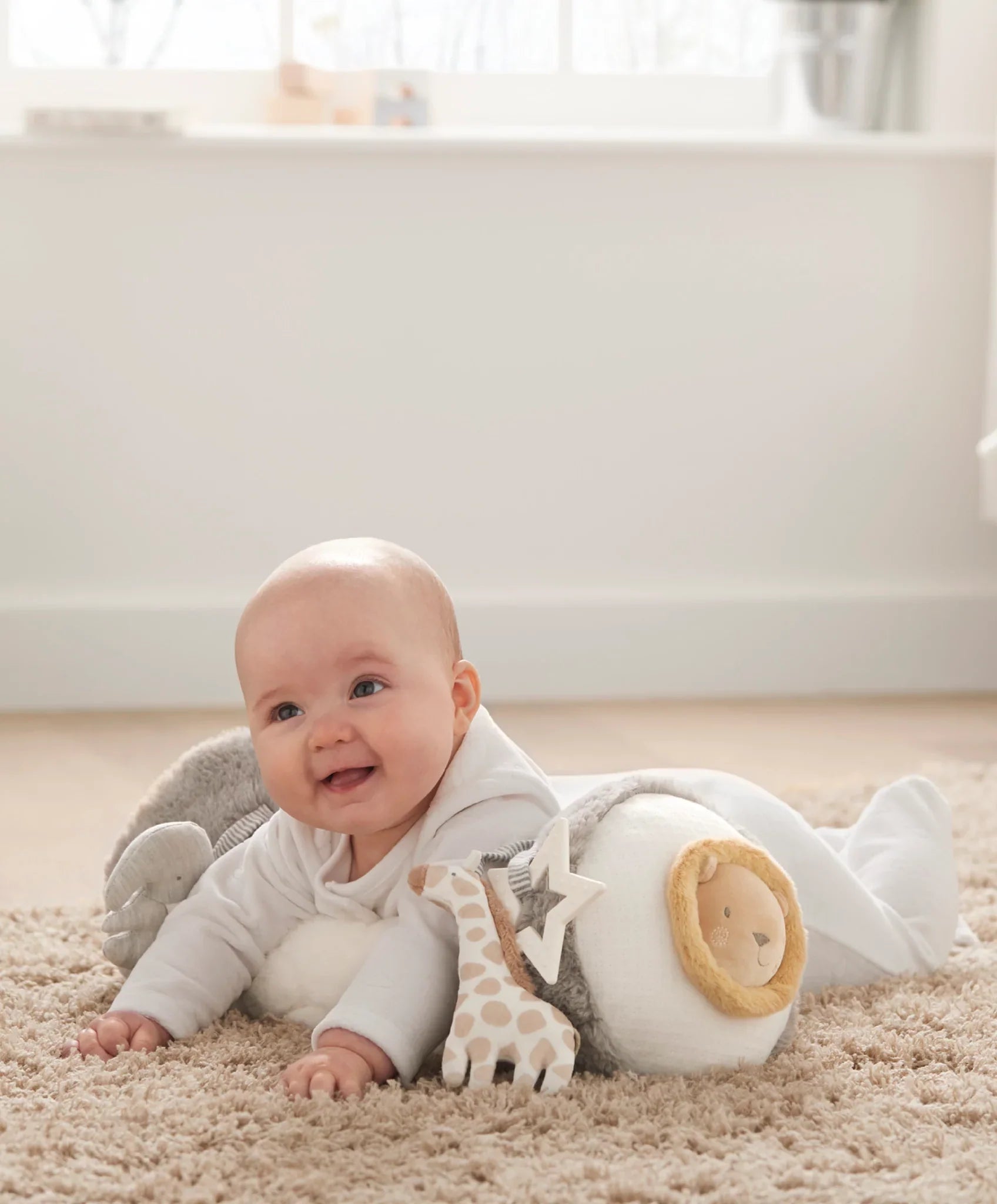 Smiling baby with plush toys using Mamas & Papas Tummy Time Roll Toshi Baby