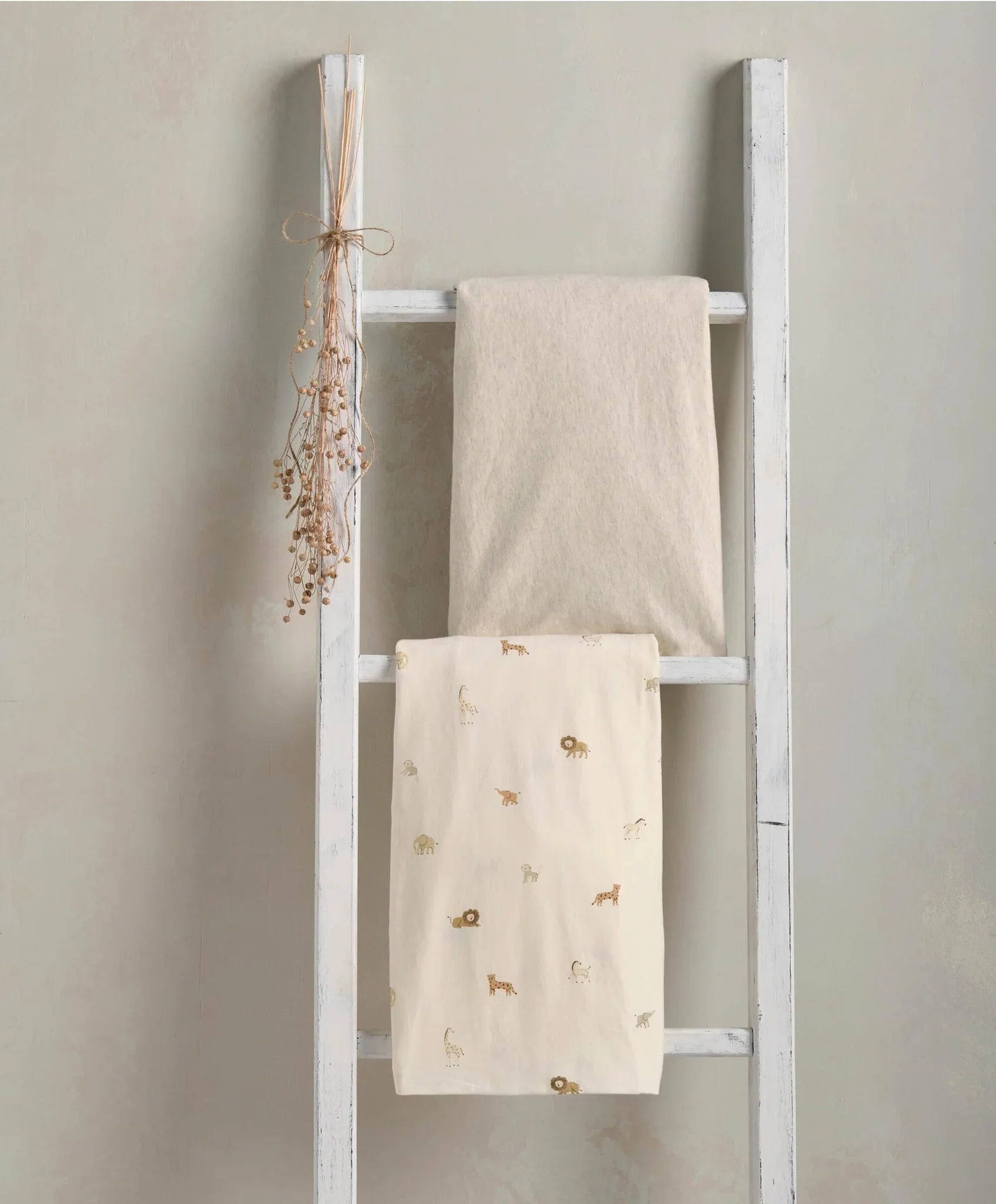 White decorative ladder with folded blankets for wild safari and marl fitted sheets setup