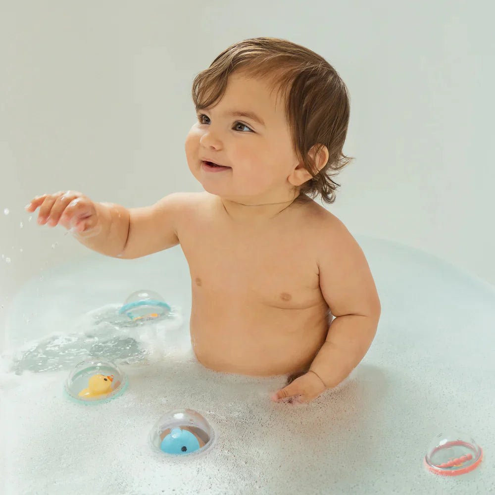 Smiling baby in a bubble bath with Munchkin Float & Play Bubbles, perfect for toshi baby rompers