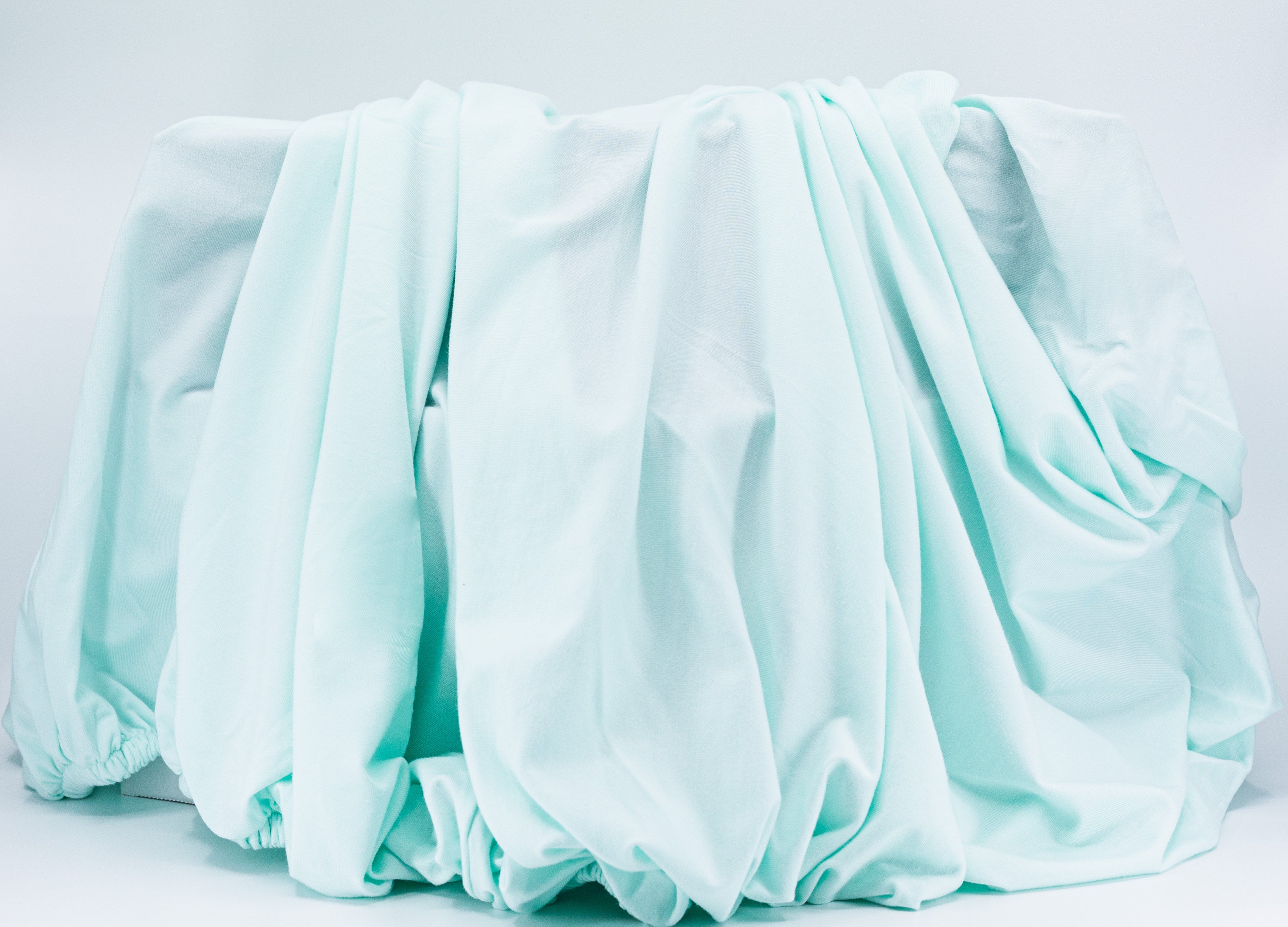 Wrinkled light blue Tasman Eco Fitted sheet draped over a baby stroller or toshi baby romper