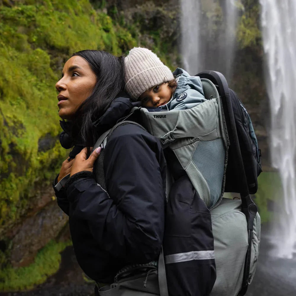 Mother carrying child in Thule Sapling Child Carrier with machine washable seat and Toshi baby gear compartmen