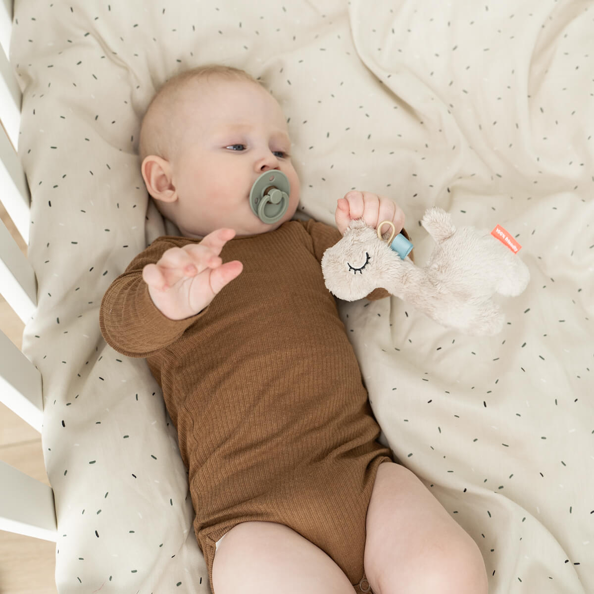 Baby in brown bodysuit with pacifier and plush toy using Done by Deer Tiny Sensory Rattle