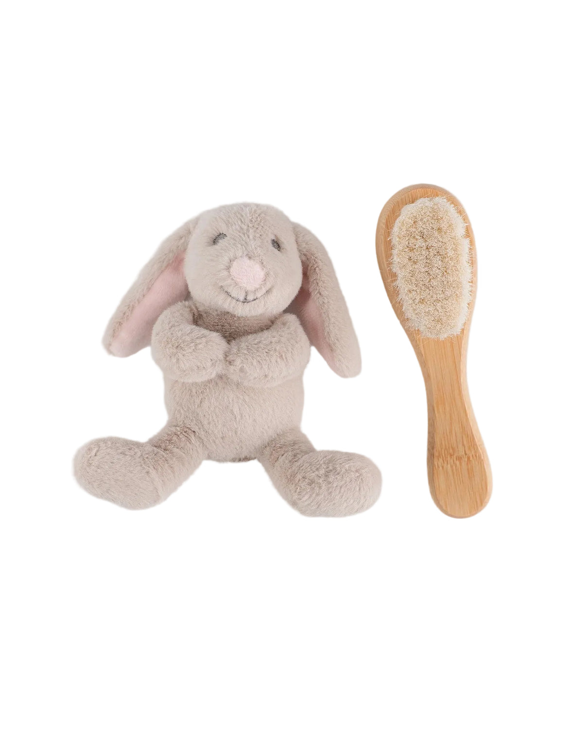 A plush bunny toy in light beige with pink inner ears and nose, shown next to a small wooden baby brush with beige bristles, on a light gray background.
